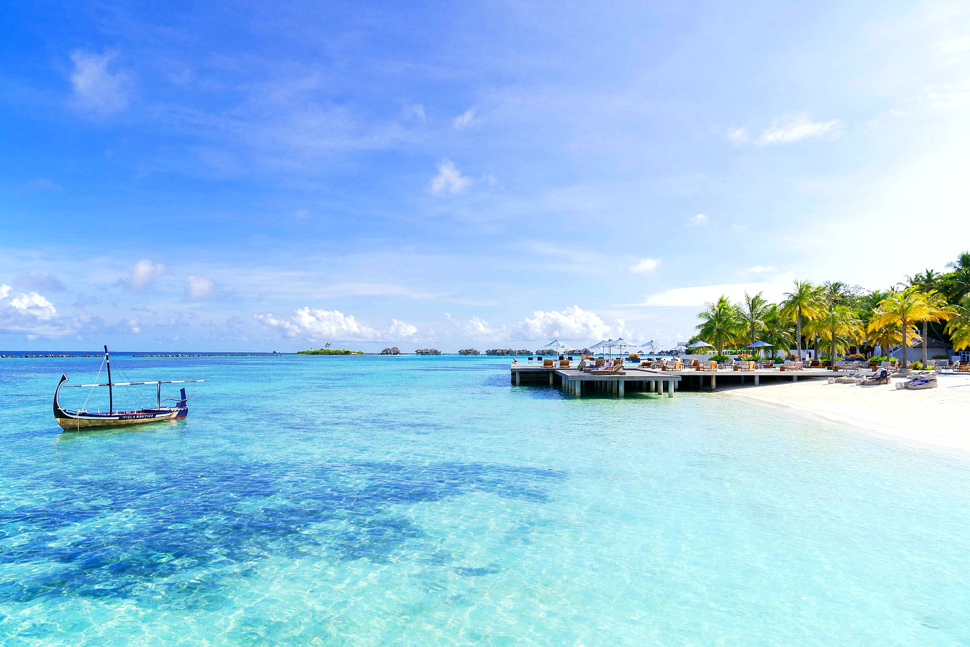 A clear turquoise lagoon with a traditional dhoni boat, a white beach and palm trees in the Maldives